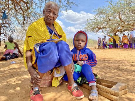 An elderly woman sits under a huge tree with her grandchild to shield from the scorching sun.